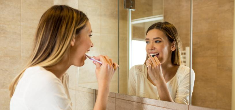 young woman brushing her teeth and looking in the mirror