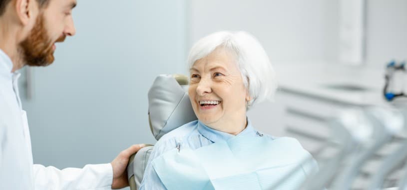 Elderly woman seated in dentist chair, smiling at dentist